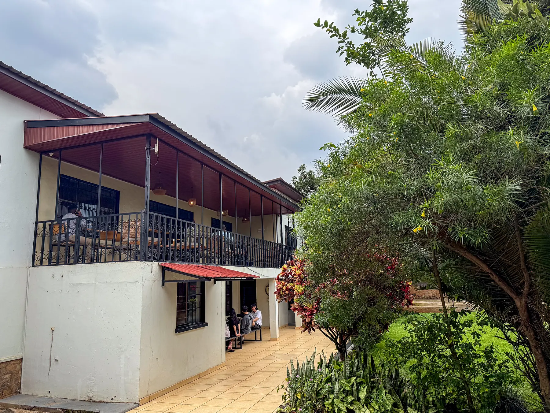 Two-storey white cafe building with covered upstairs balcony seating and tropical garden at Question Coffee in Kigali, Rwanda