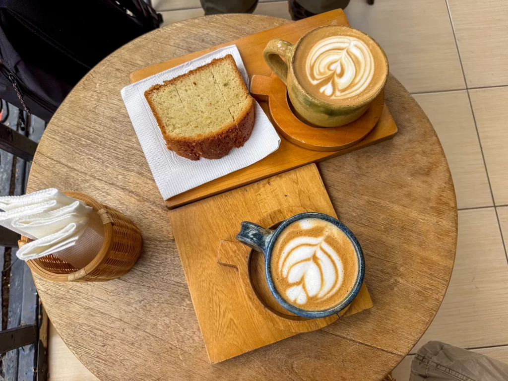 Two latte art coffees and a slice of yellow cake on a wooden table at Question Coffee in Kigali, Rwanda