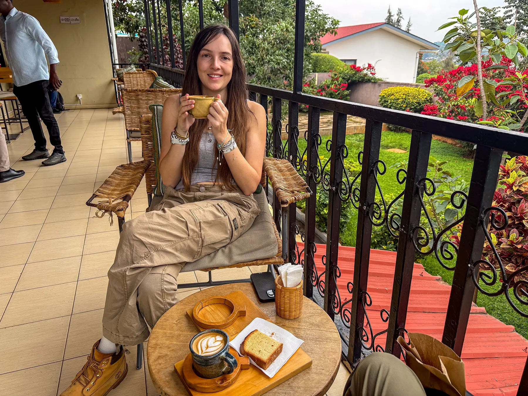 Ella McKendrick holding a cappuccino at a terrace table with cake and latte at Question Coffee in Kigali, Rwanda