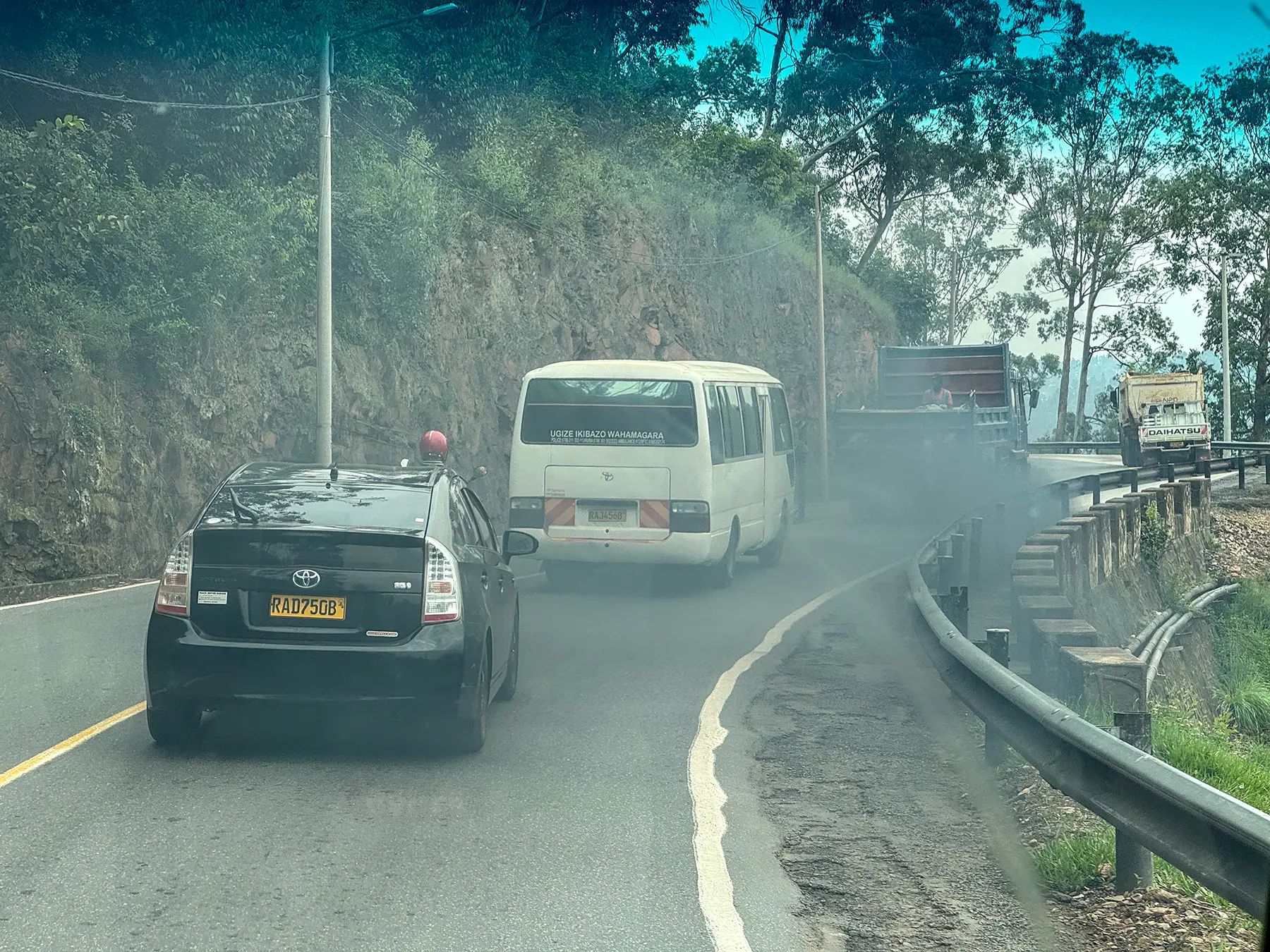 Minibus and car climbing winding hillside road in exhaust haze at Northern Province, Rwanda