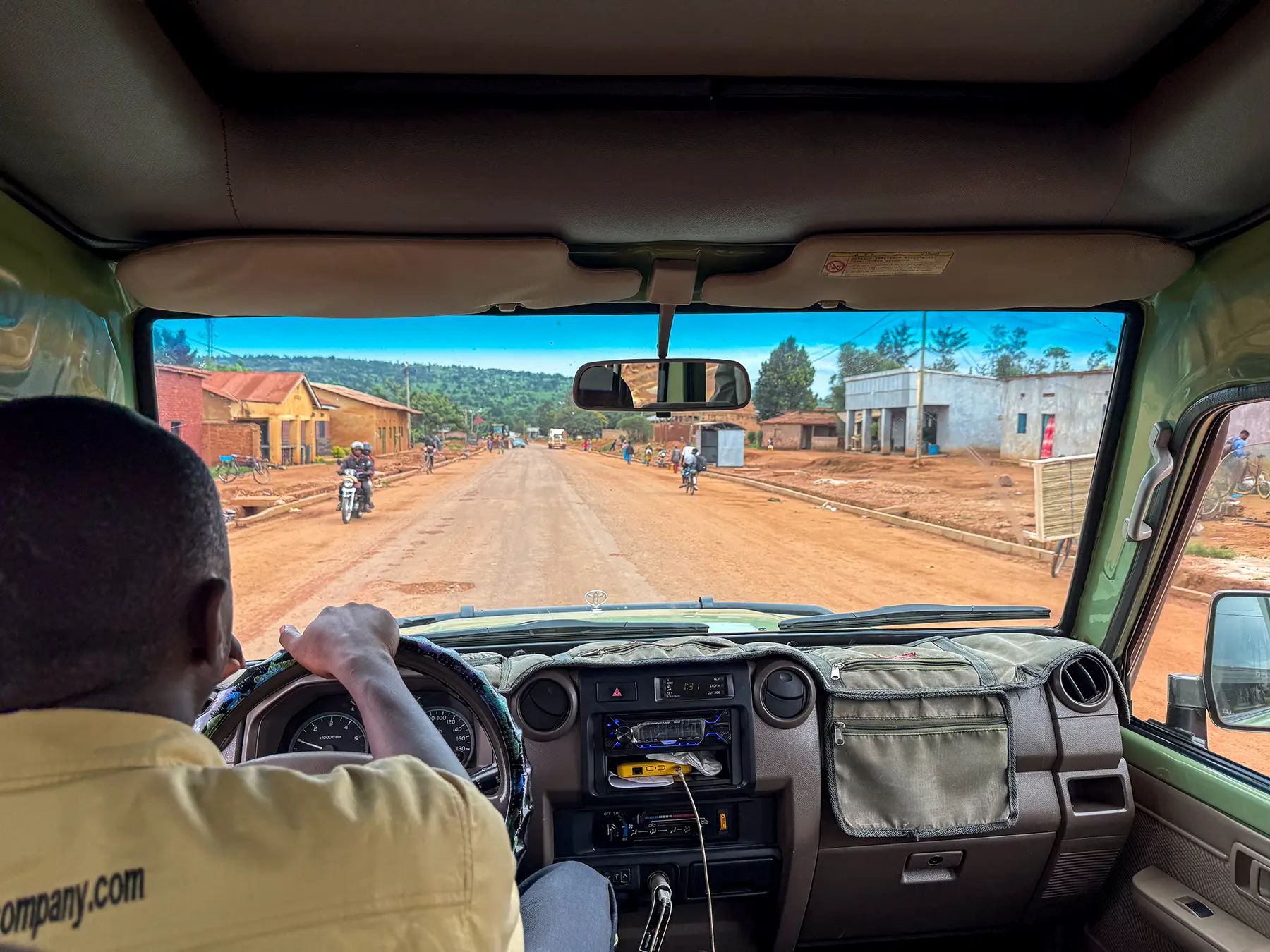 View through safari vehicle windscreen of dirt road and town at roadside in Rwanda