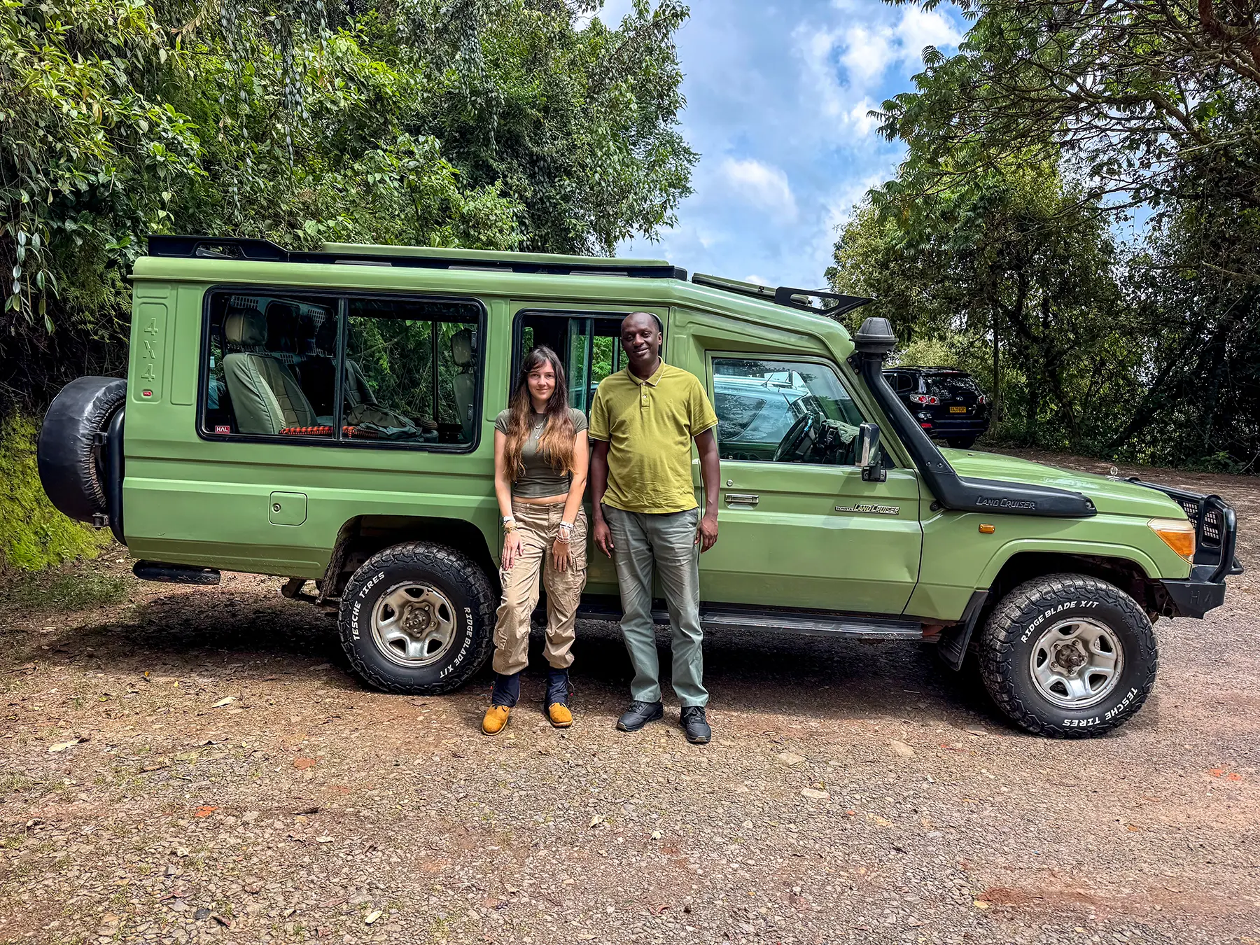 Ella McKendrick with a local tour operator beside a green Land Cruiser at a safari vehicle pickup point, Rwanda