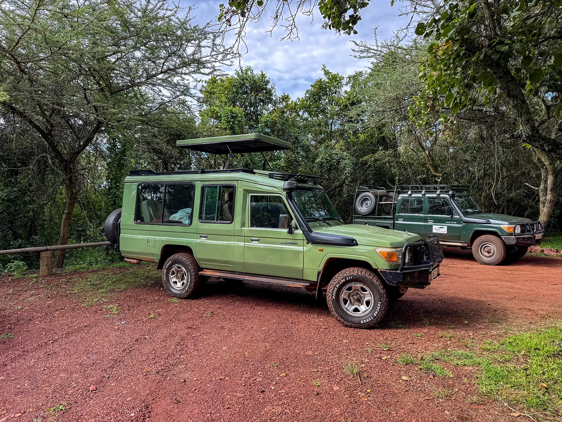 Two green Toyota Land Cruiser safari vehicles parked under trees at a safari vehicle parking area, Rwanda
