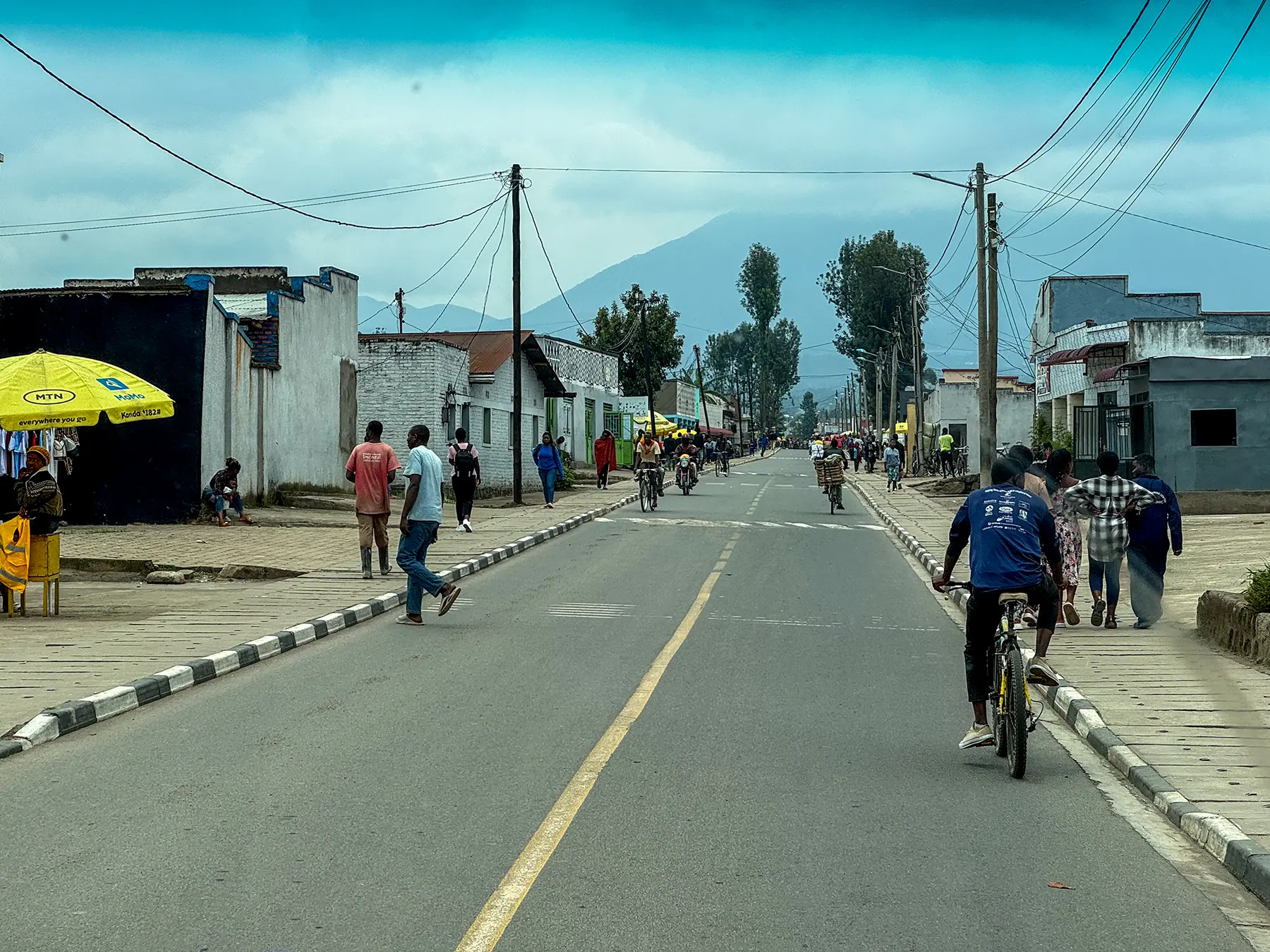 Town street with cyclists and volcano peak rising into cloud at Musanze in Volcanoes National Park, Rwanda