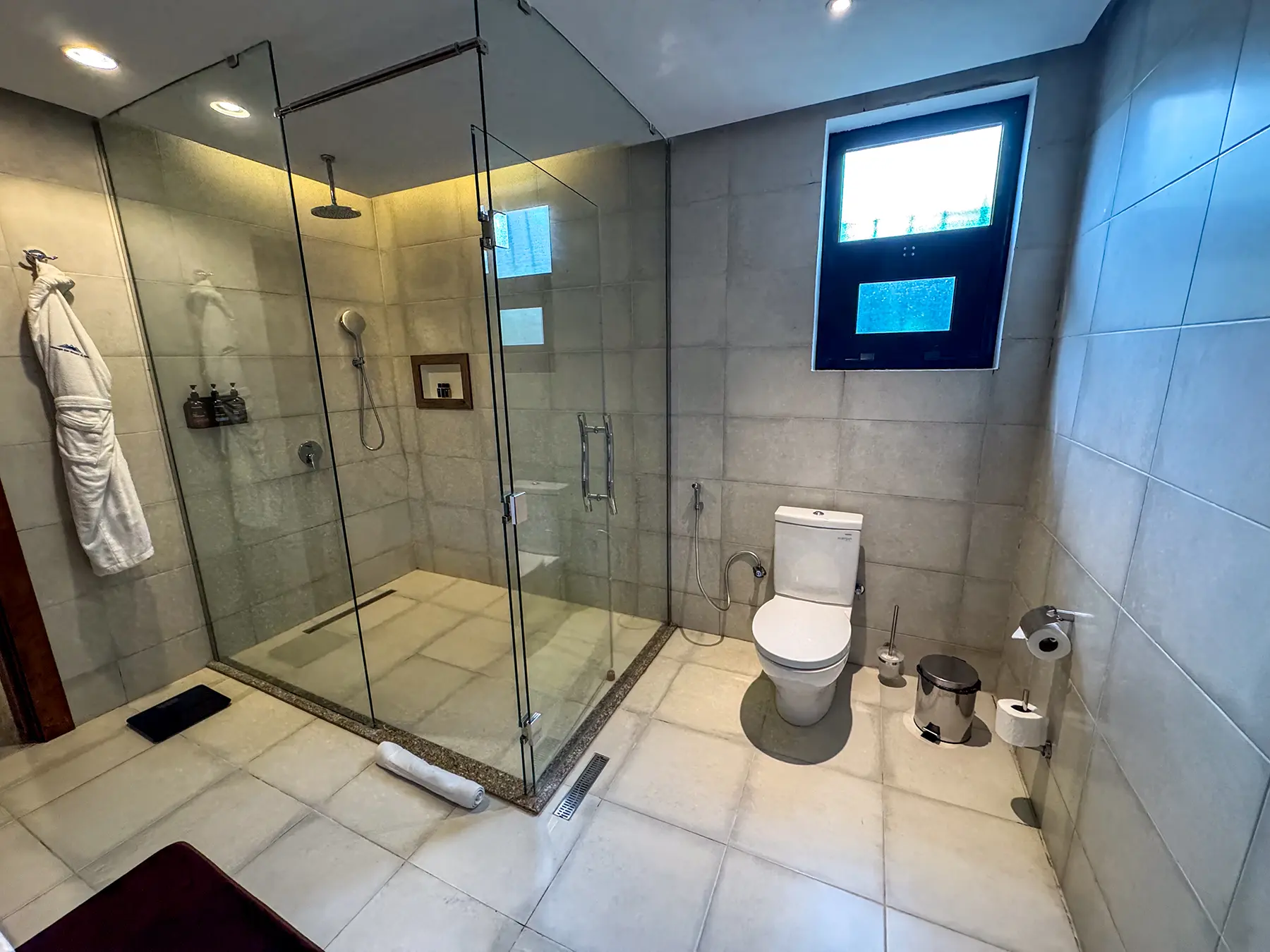 Tiled bathroom with glass walk-in shower, robe and toilet at Virunga Inn in Volcanoes National Park, Rwanda