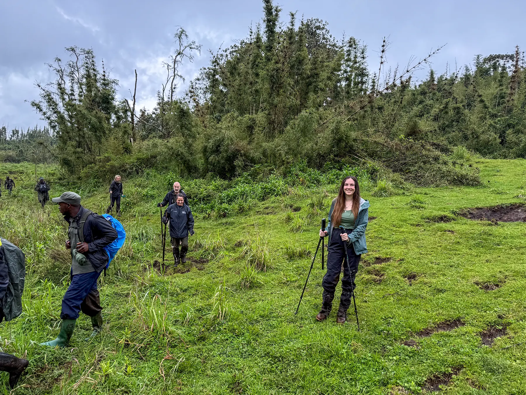 Ella McKendrick smiling with trekking group and guides crossing a green meadow at the high meadow in Volcanoes National Park, Rwanda