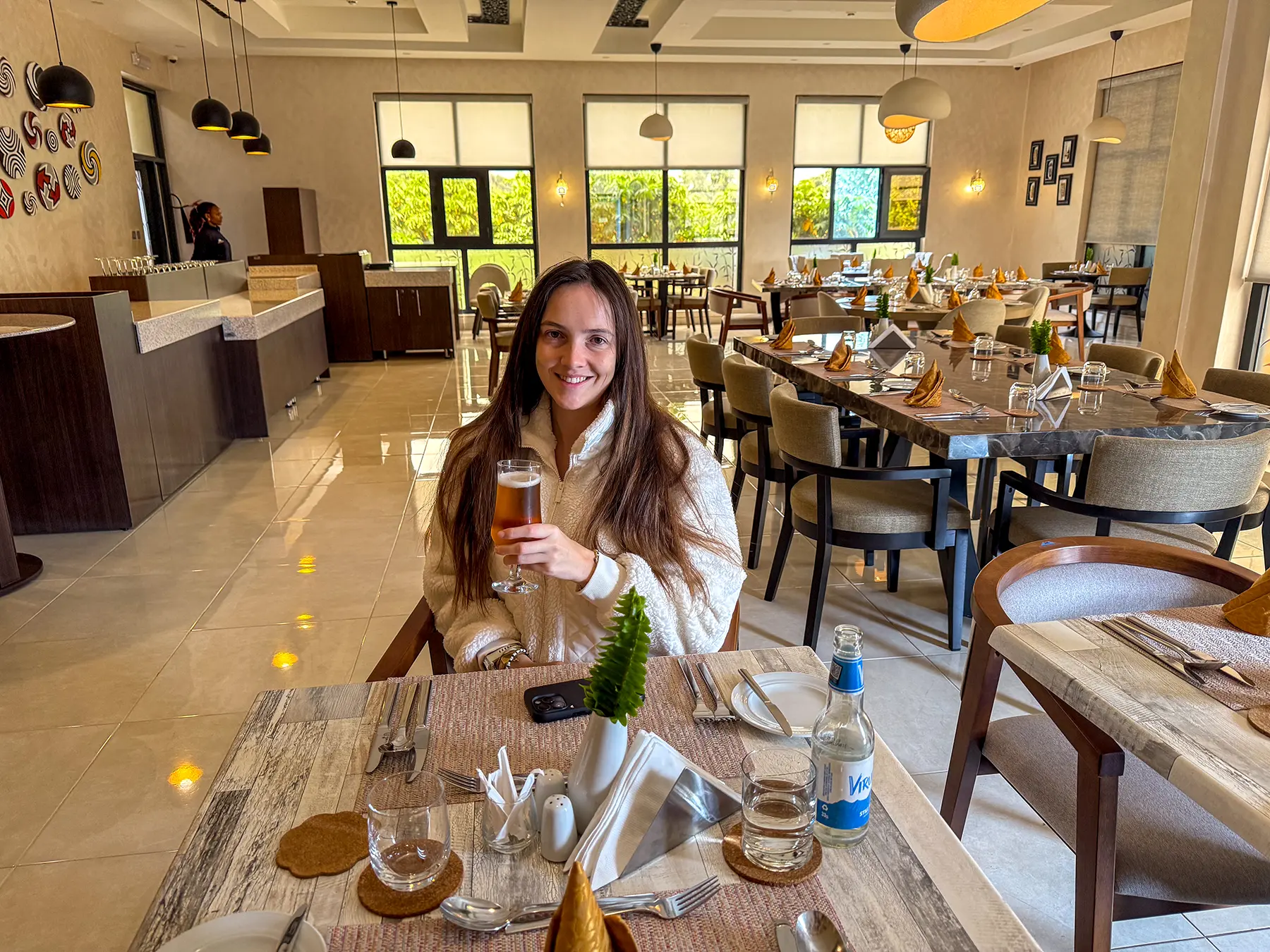 Ella McKendrick holding a beer at a set dining table in the restaurant at Virunga Inn in Volcanoes National Park, Rwanda