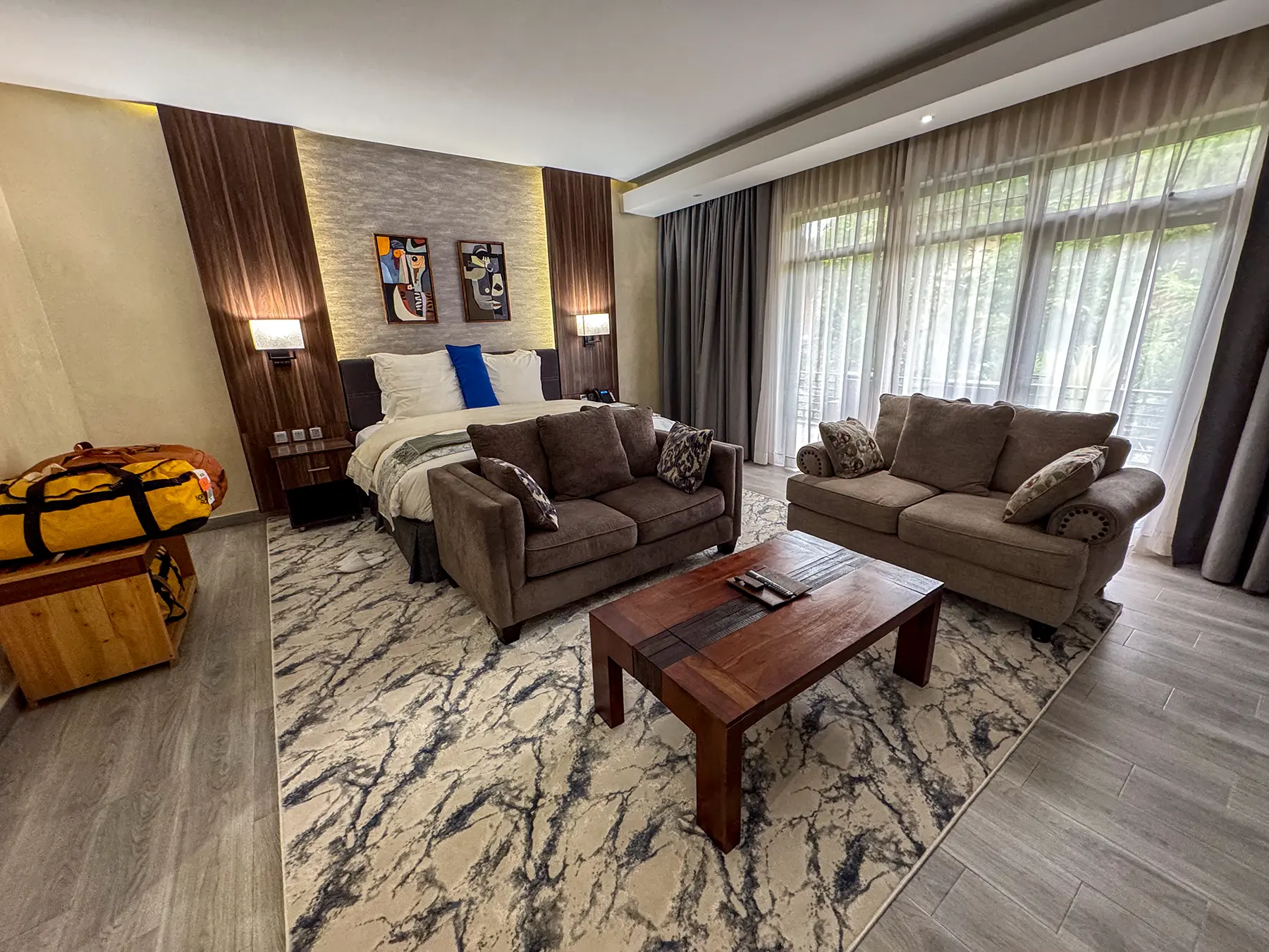 Bedroom with sofas, coffee table and yellow duffel on marble-pattern rug at Virunga Inn in Volcanoes National Park, Rwanda