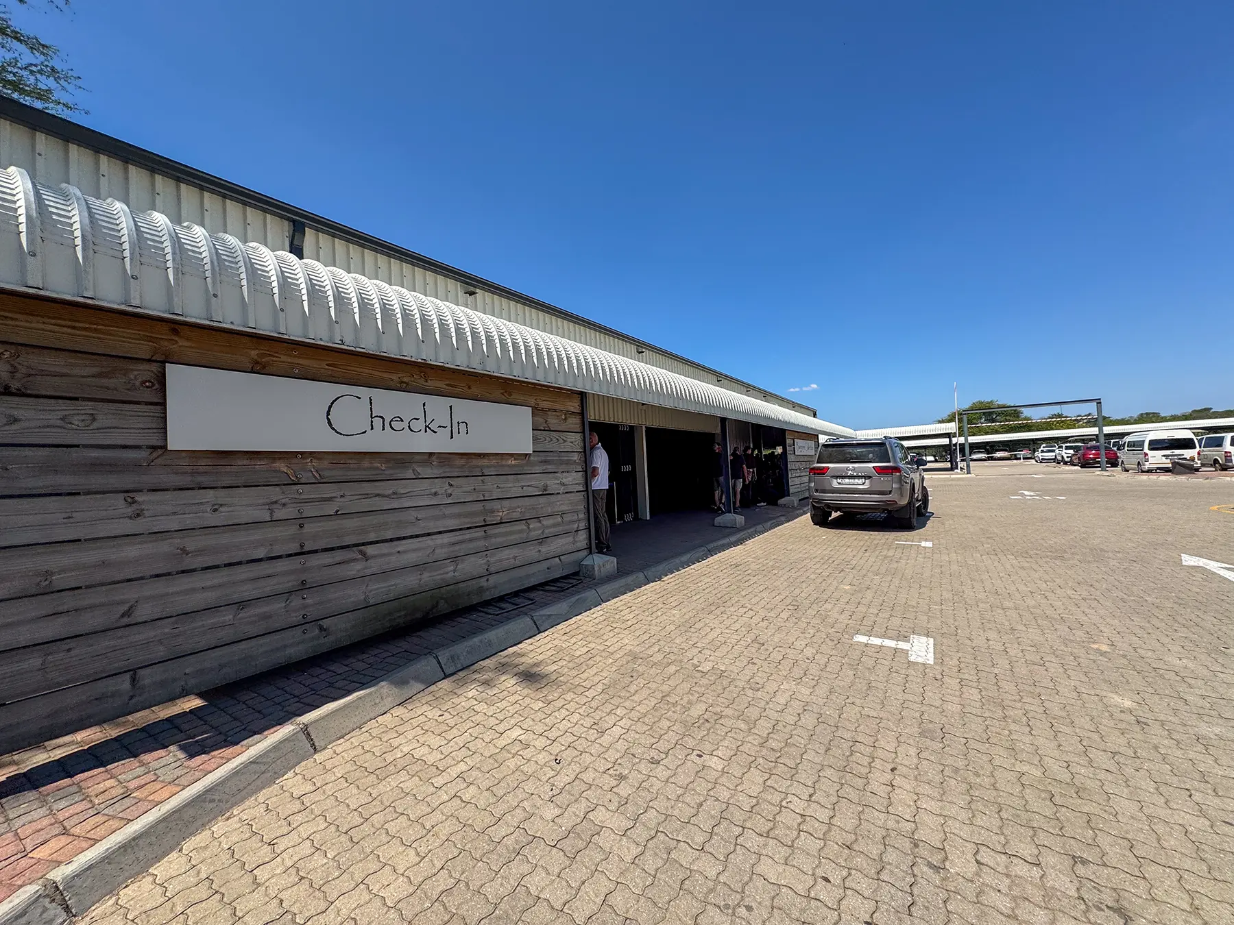 Check-In sign on the timber terminal wall with travellers at the entrance at Hoedspruit Eastgate Airport in Hoedspruit, South Africa