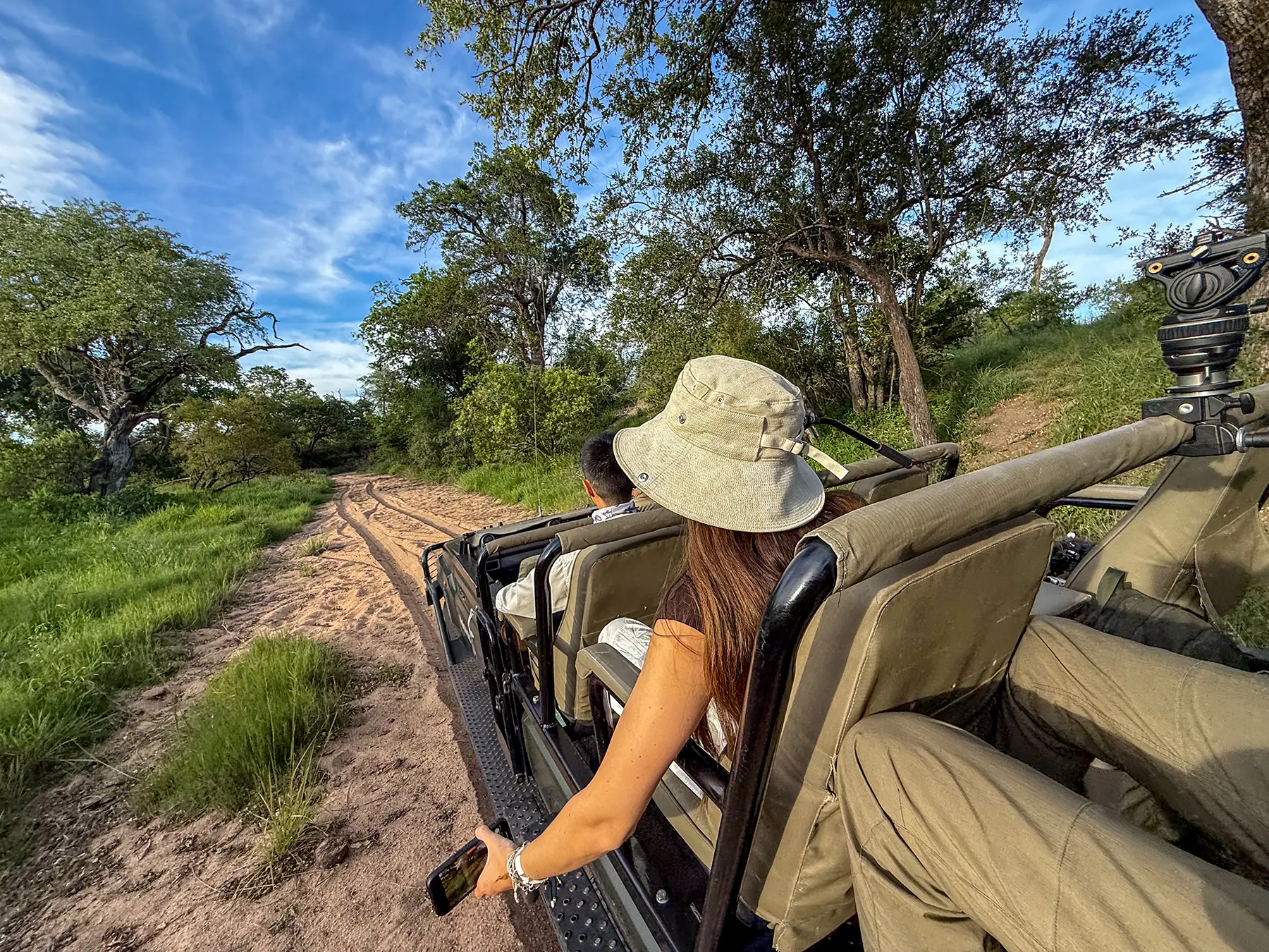Ella McKendrick holding a phone from an open safari vehicle on a sandy track on safari in MalaMala Game Reserve, South Africa
