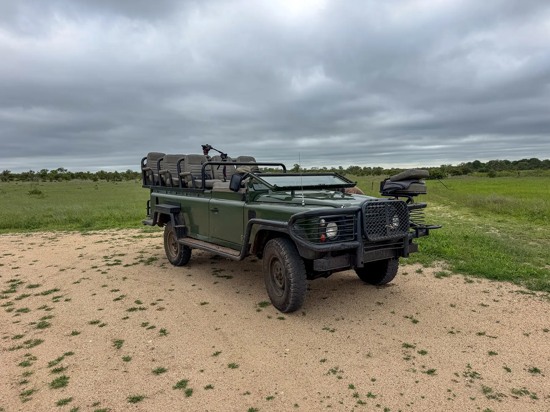Open green safari vehicle parked on bare sand under an overcast grey sky at a bush clearing in Manyeleti Game Reserve, South Africa