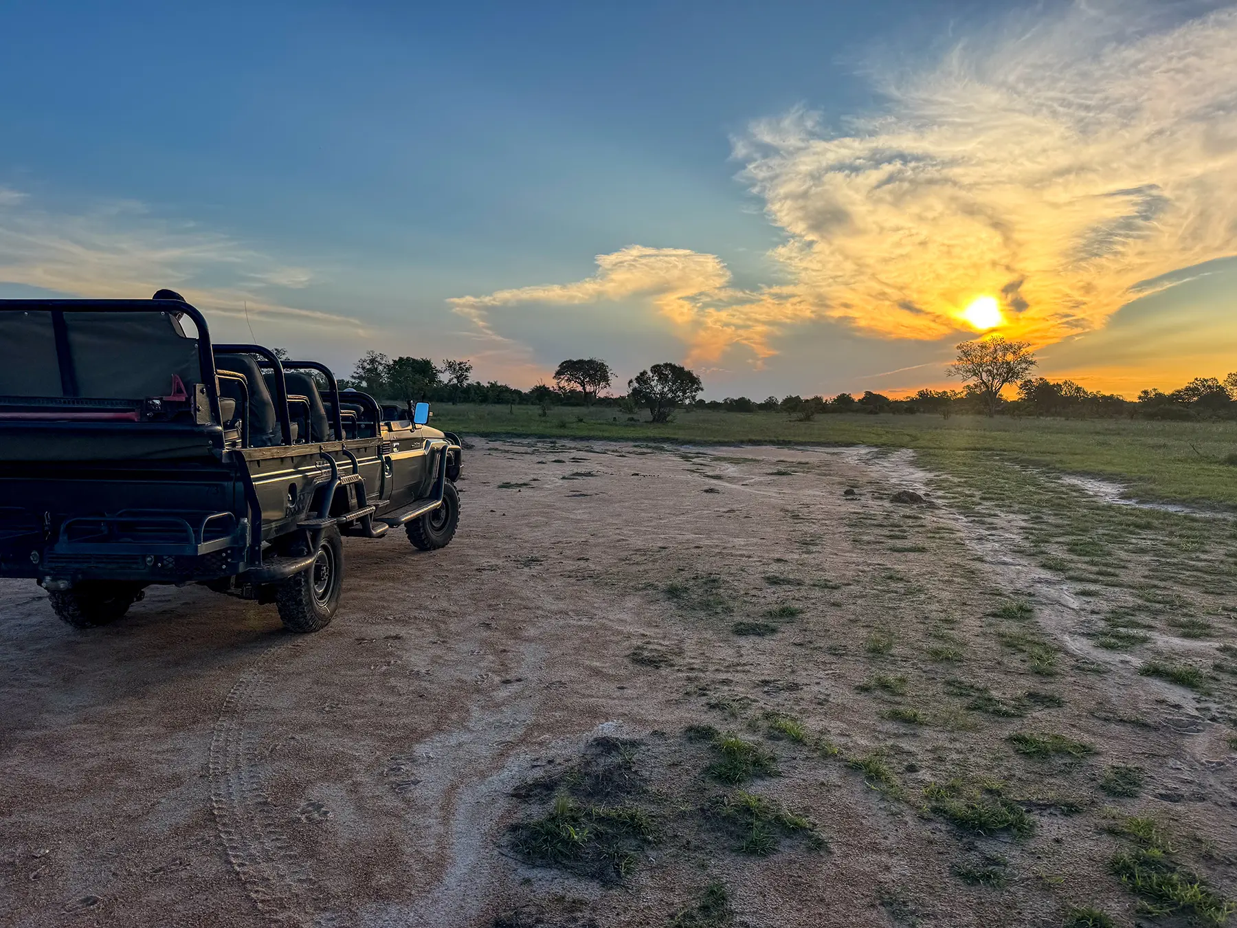 Open safari vehicle parked on the plains as the sun sets over distant trees at a bush clearing in Manyeleti Game Reserve, South Africa