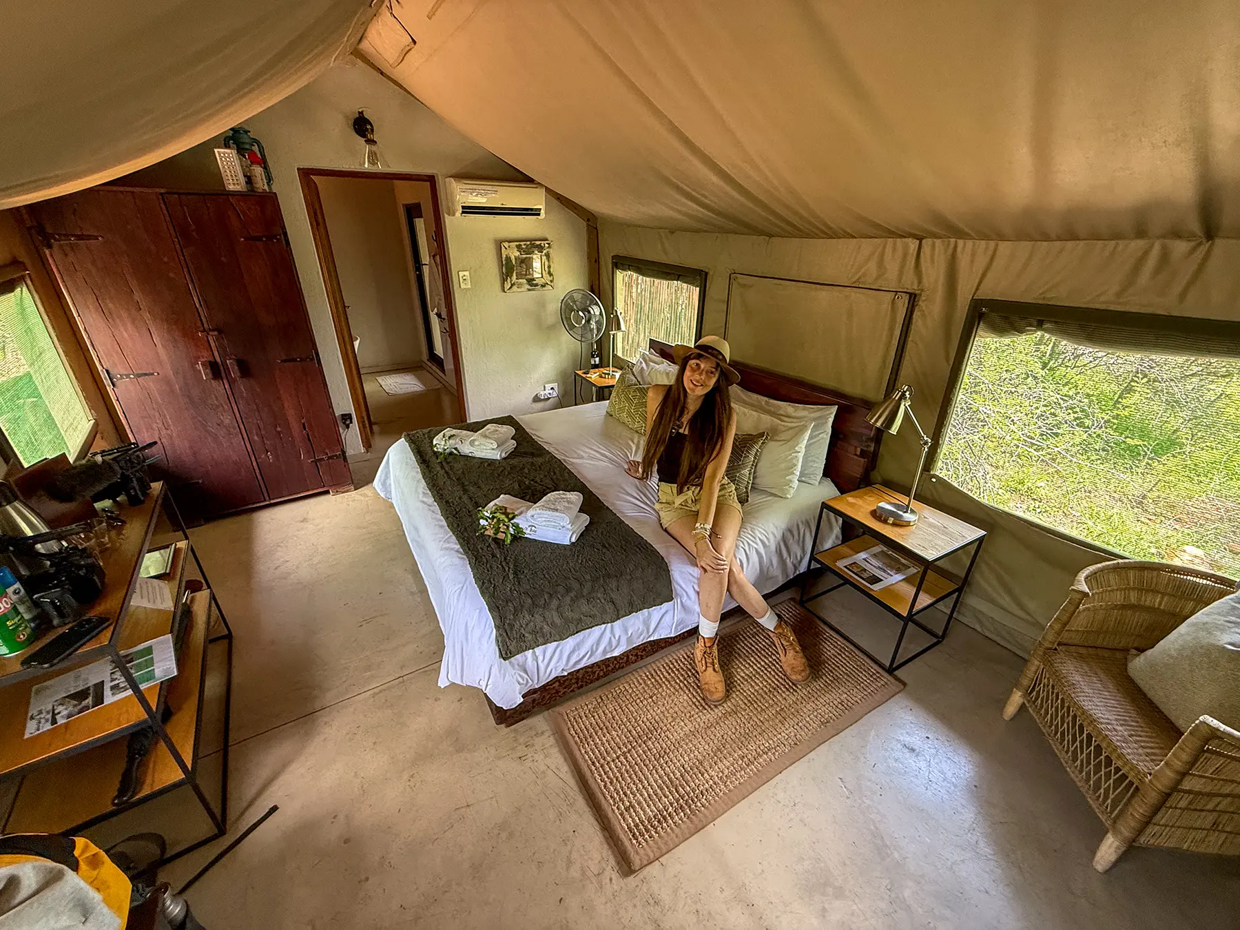 Ella McKendrick sitting on the bed inside a canvas tented room with wooden wardrobe at Sausage Tree Camp in Olifants River Game Reserve, South Africa