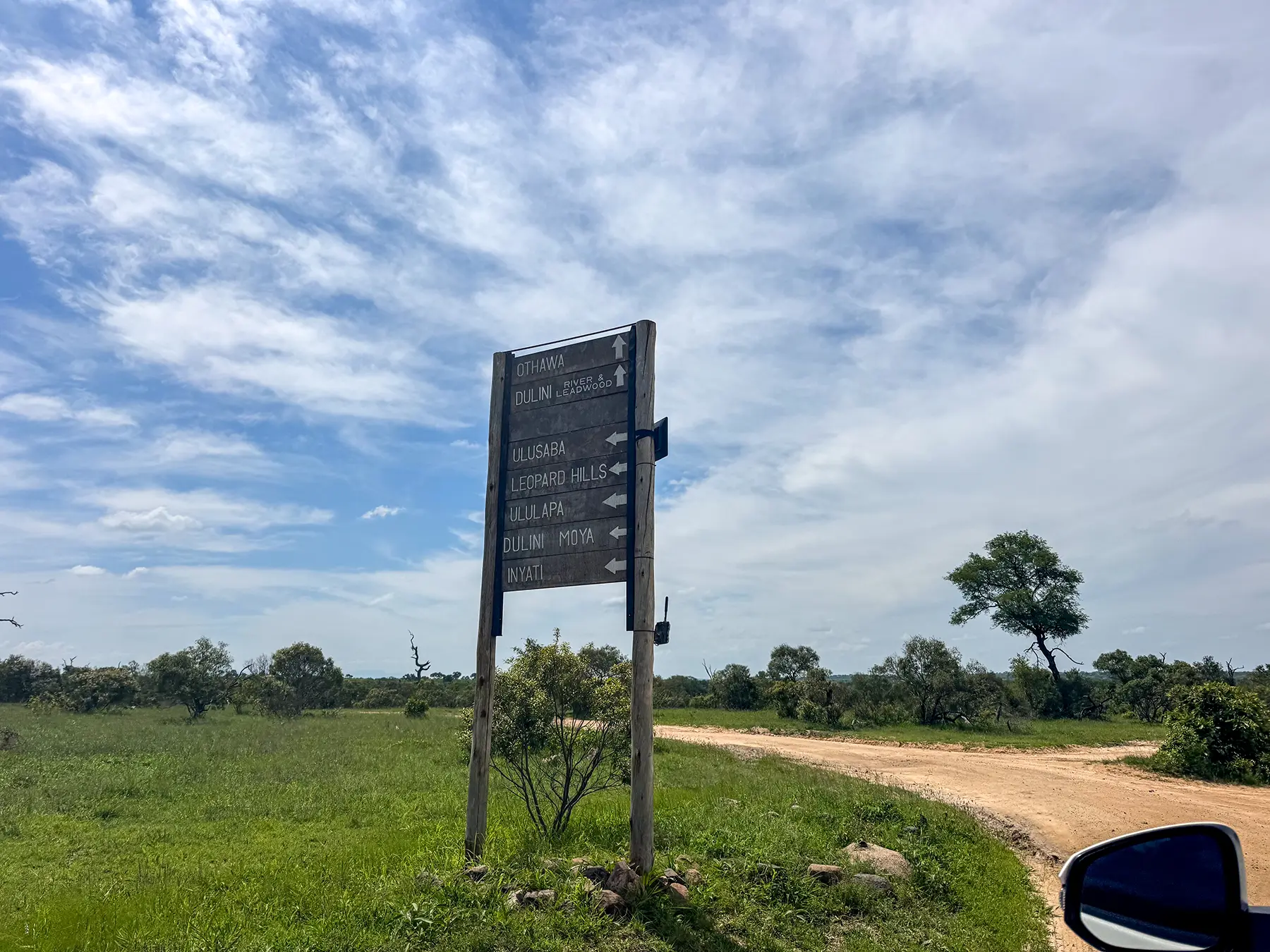 Wooden signpost pointing to safari destinations beside a dirt road at a road junction in Sabi Sand Game Reserve, South Africa