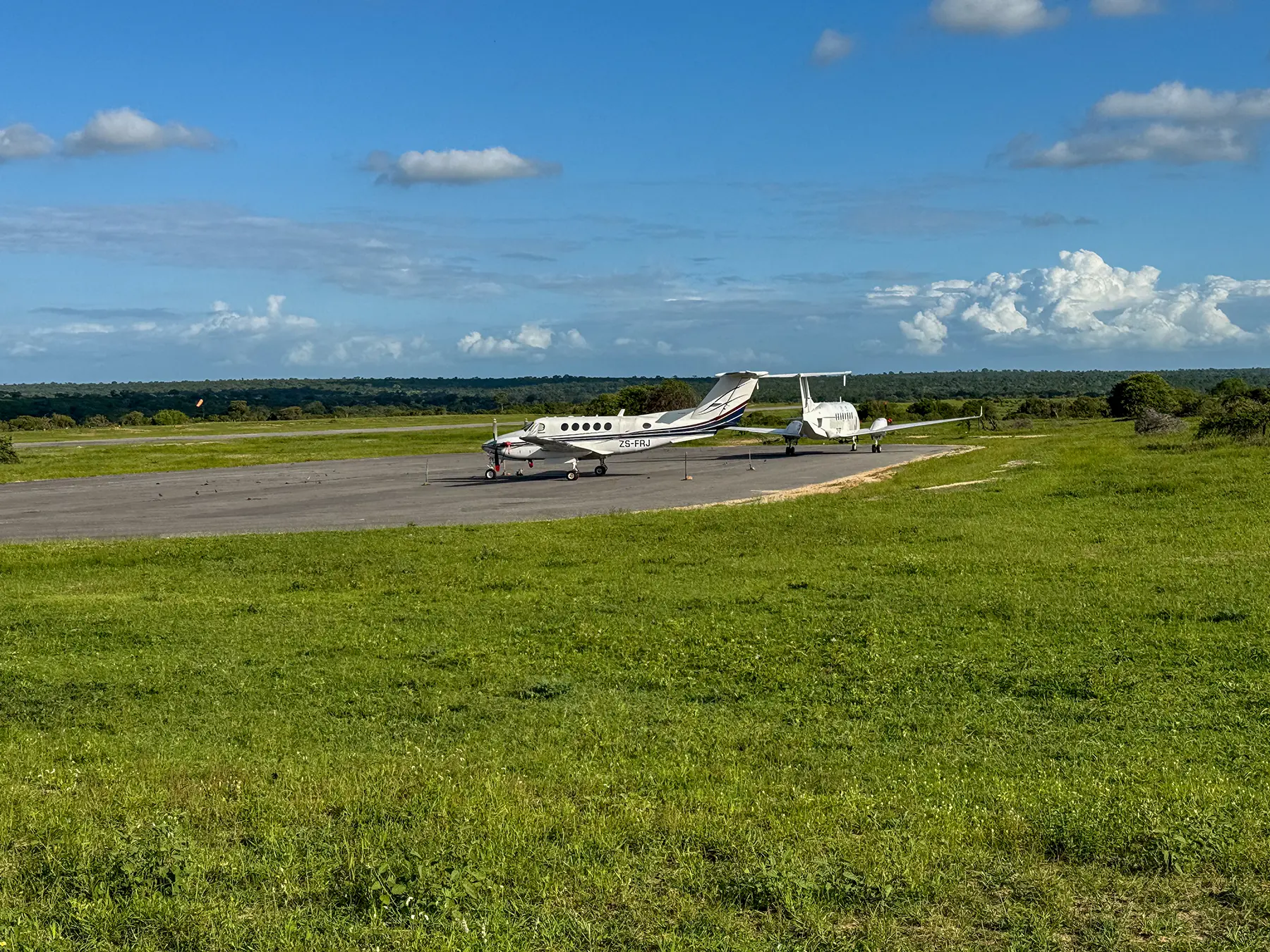 Two white propeller aircraft parked on the runway edge at a bush airstrip in South Africa