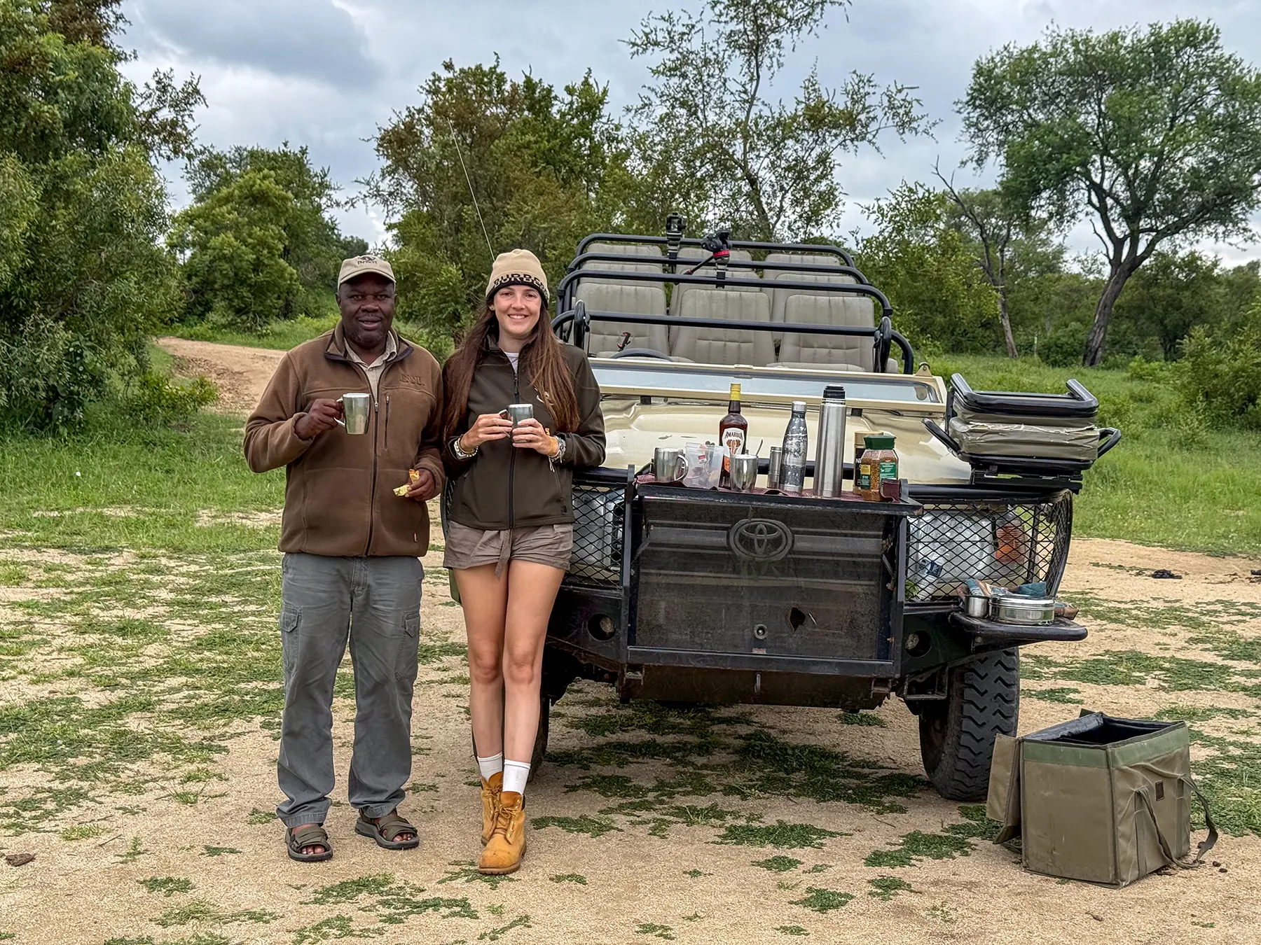 Ella McKendrick and a safari guide holding mugs by a Land Cruiser at a bush coffee stop in South Africa