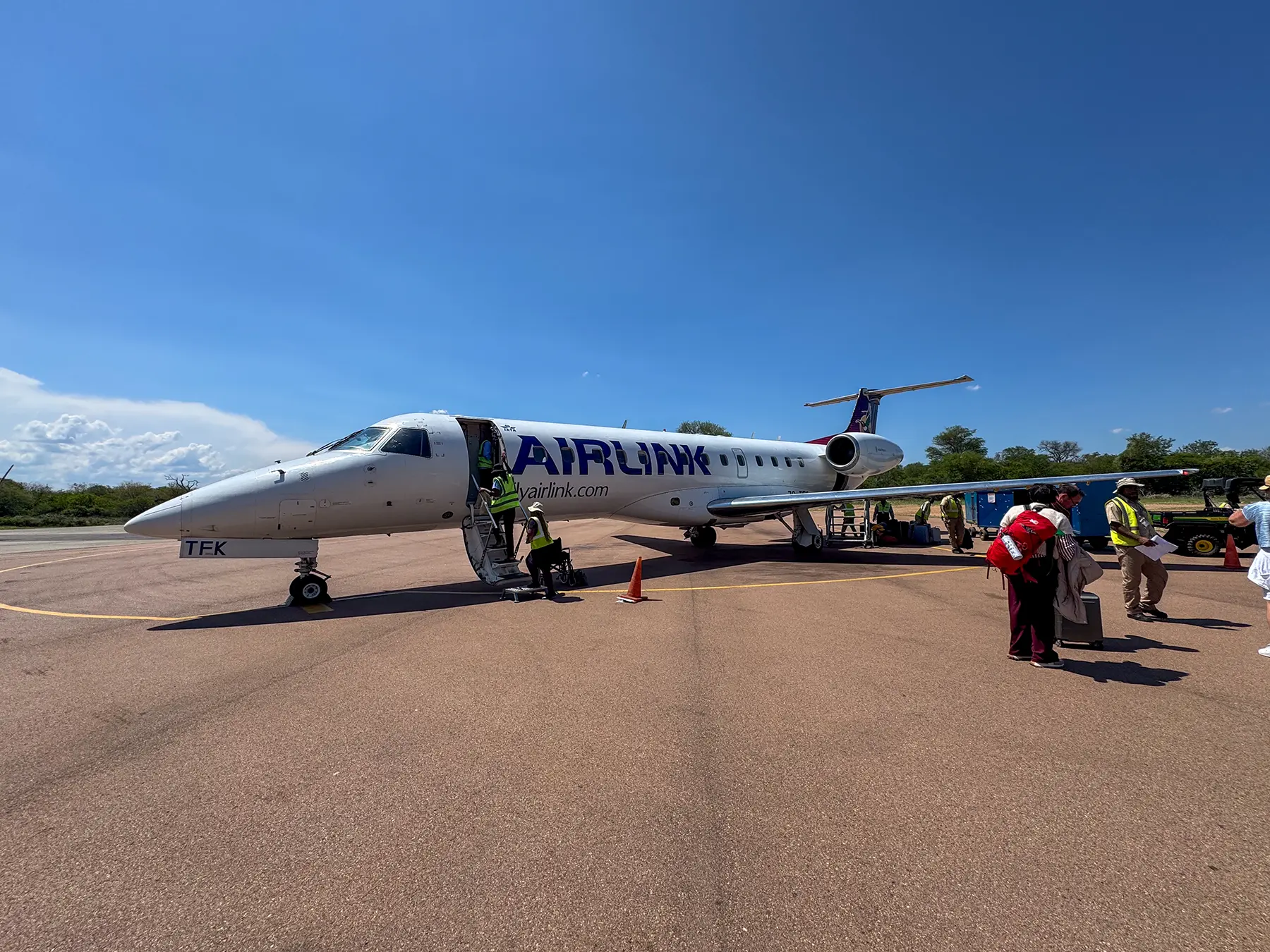 Passengers and ground crew boarding an Airlink jet at a rural airport apron in South Africa