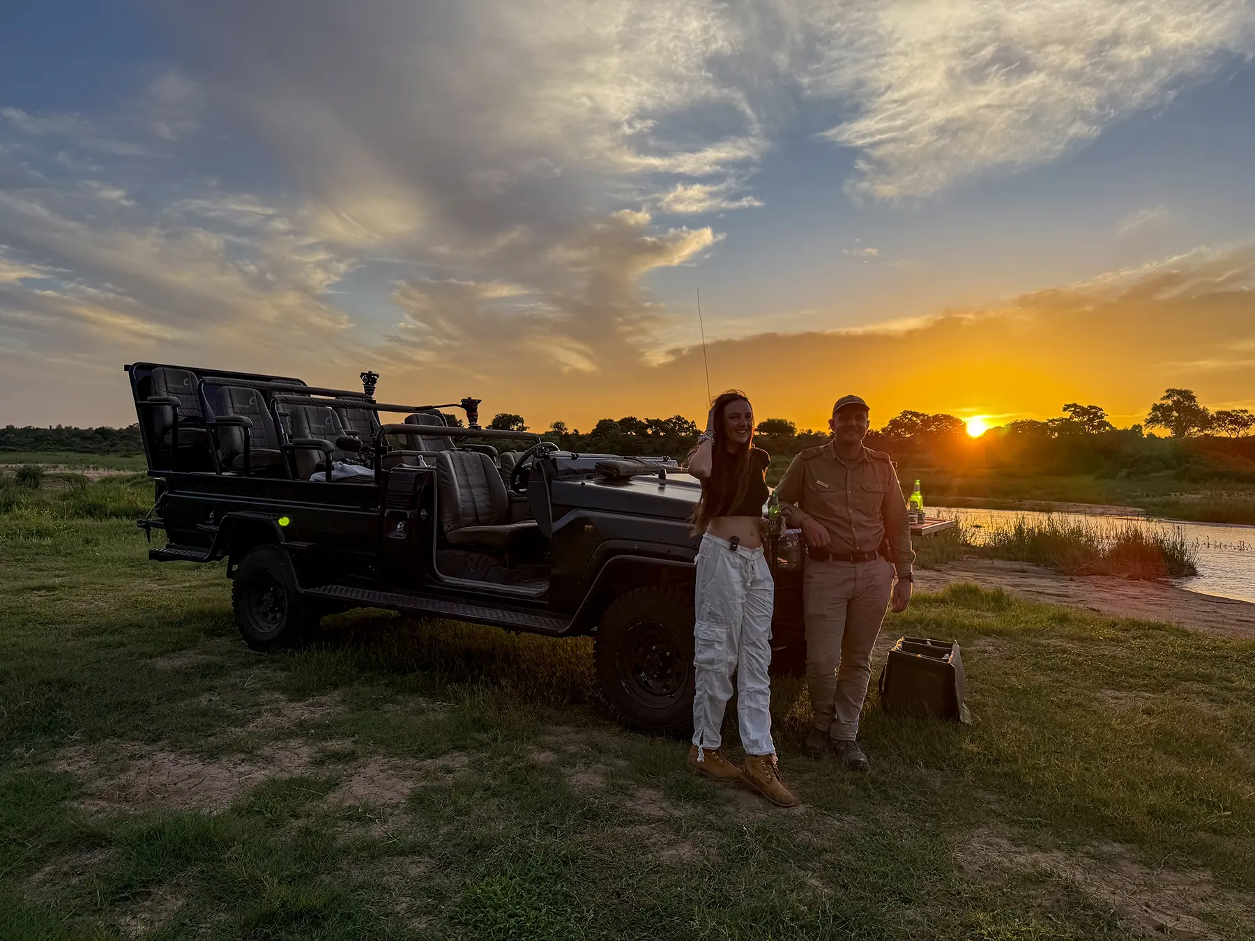Ella McKendrick and a safari guide next to a safari truck at a riverside sundowner stop in South Africa