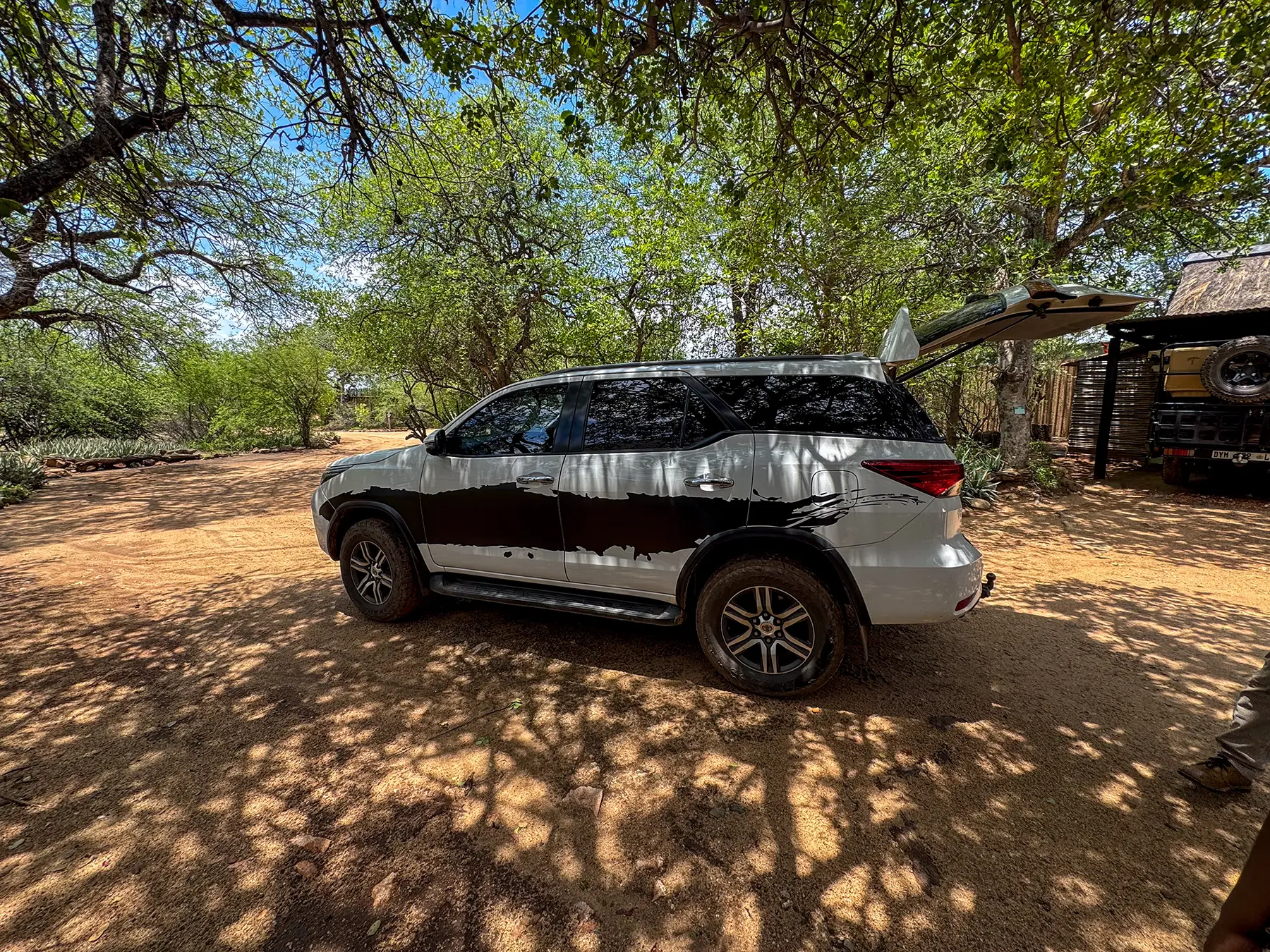 White SUV with raised tailgate parked on sandy ground at a shaded parking area in South Africa