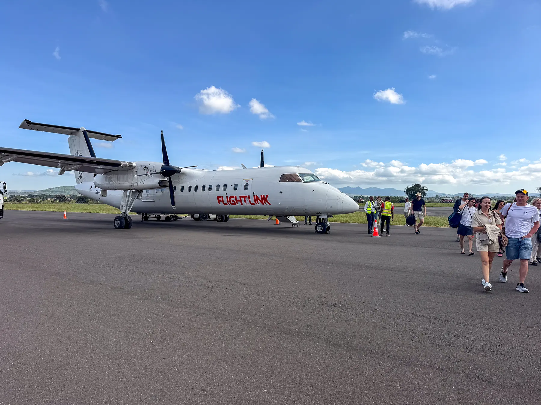 Propeller aircraft which had taken us from Zanzibar, parked on the apron as passengers walk away past ground crew at Arusha Airport in Arusha, Tanzania