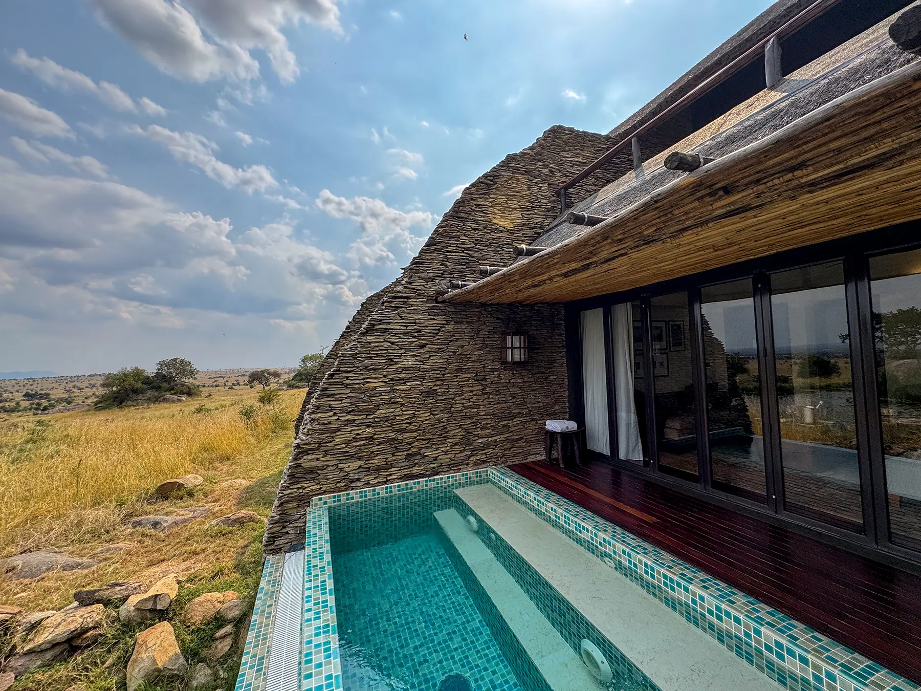 Private pool beside stone-clad villa with thatched roof above open plains at Four Seasons Safari Lodge Serengeti in Serengeti National Park, Tanzania