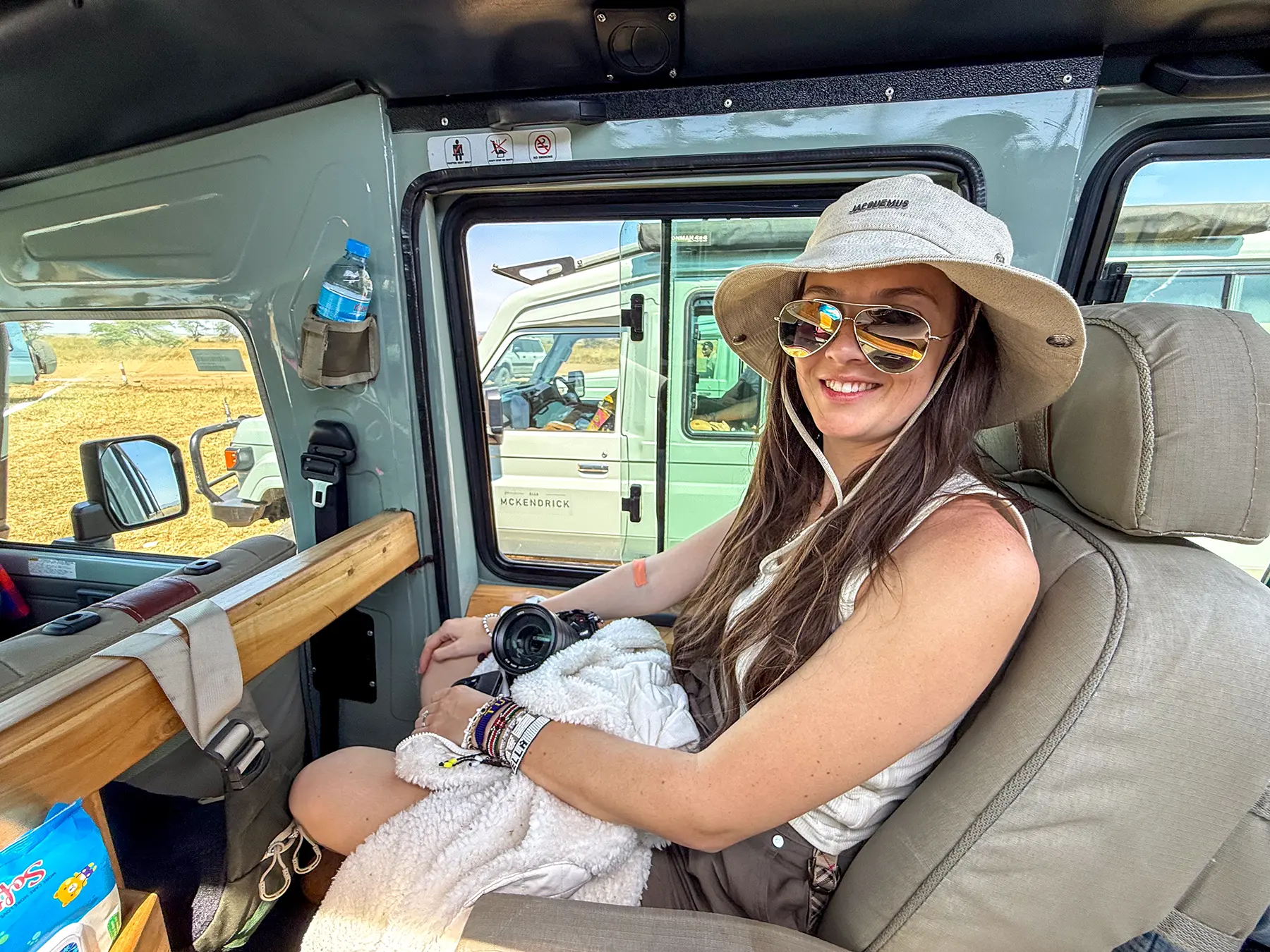 Ella McKendrick seated with camera inside Land Cruiser beside another safari vehicle on safari in Serengeti National Park, Tanzania