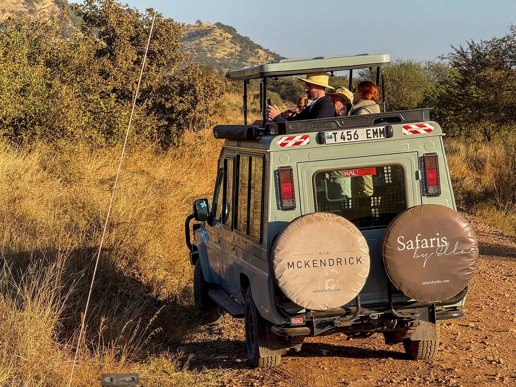 Rear of a safari Land Cruiser with travellers standing under raised roof on safari in Serengeti National Park, Tanzania