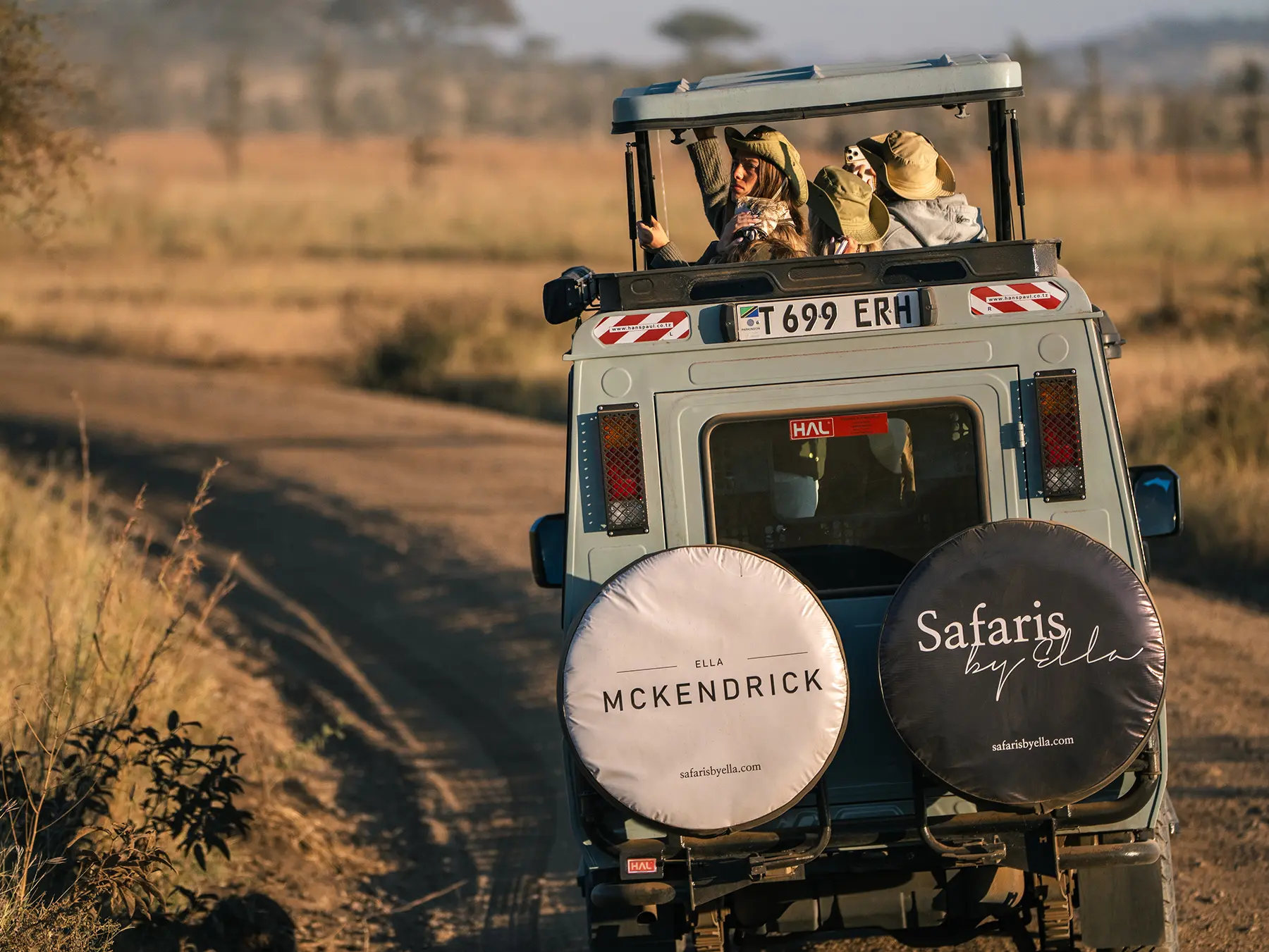 Travellers standing in the pop-top roof of a Land Cruiser on safari in Serengeti National Park, Tanzania