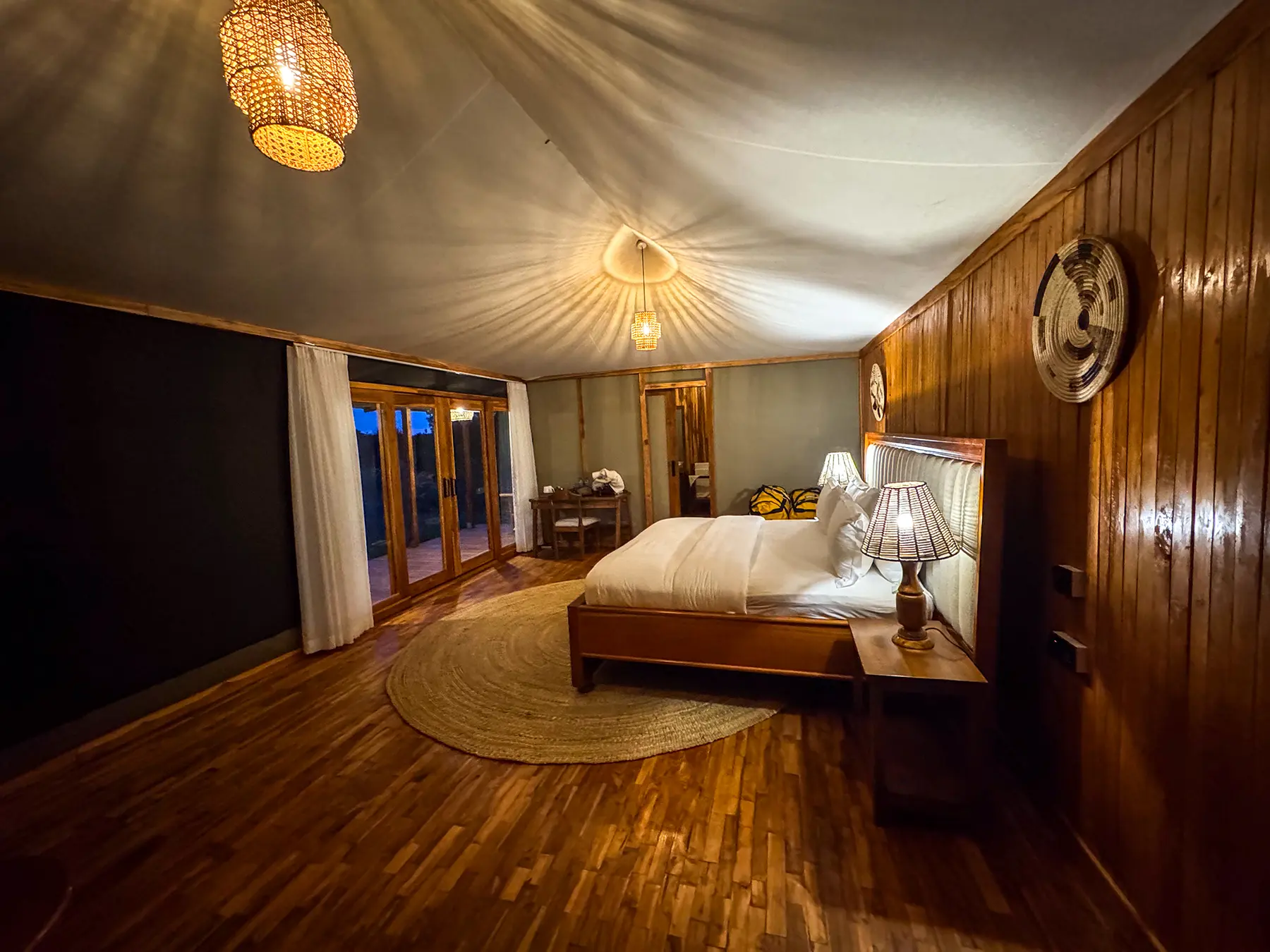 Bed, desk and glass doors opening onto the deck inside a canvas-roofed room at Tarangire Safari Haven in Tarangire National Park, Tanzania