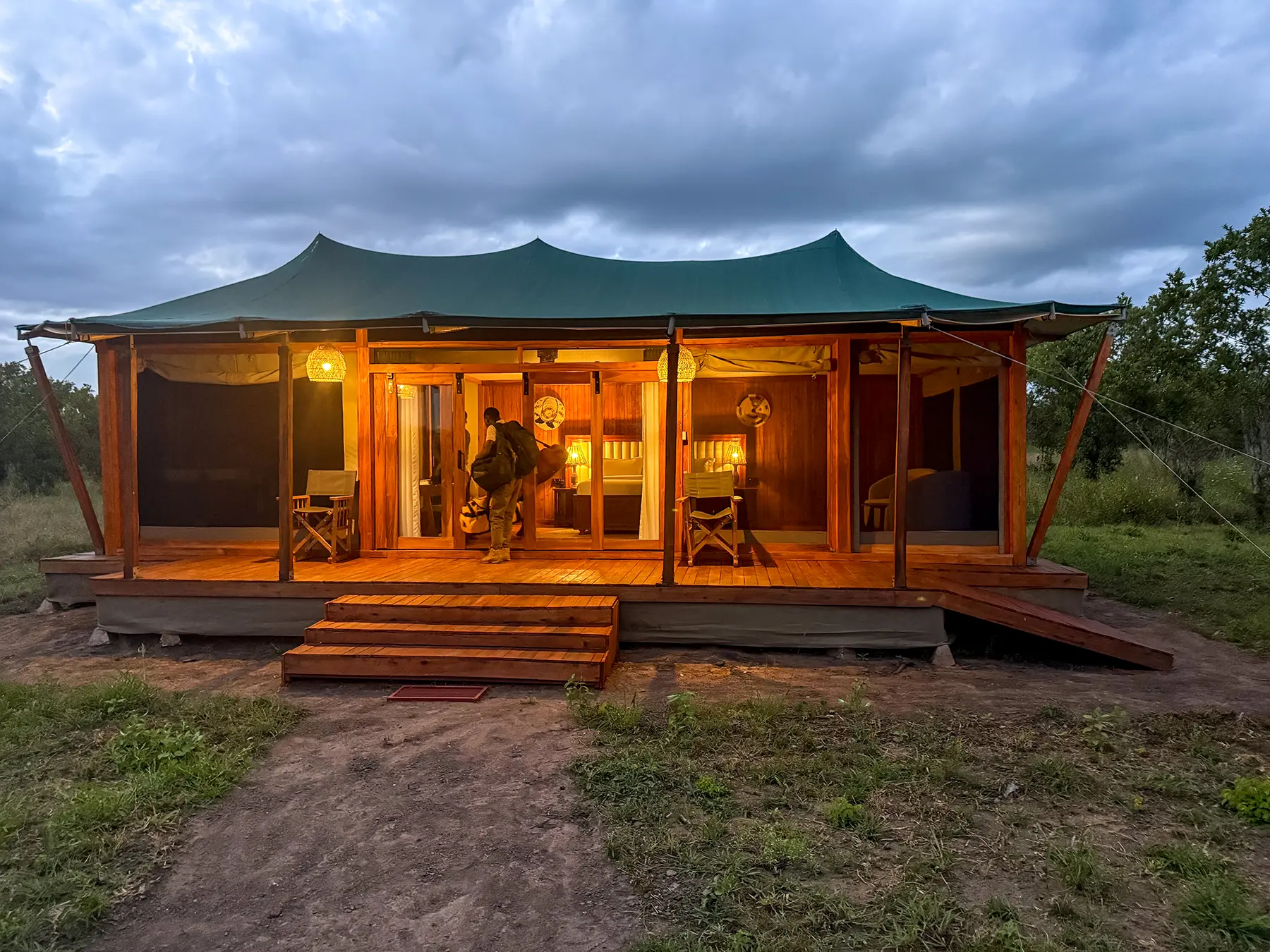 Staff member carrying our bags into a lamplit canvas-roofed room with timber deck at Tarangire Safari Haven in Tarangire National Park, Tanzania