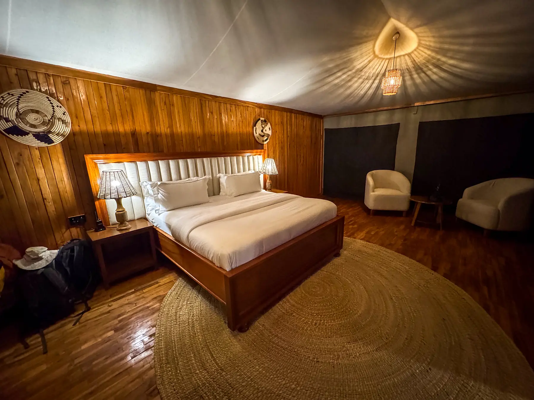 Bed, woven wall baskets and round rug in timber-walled canvas-roofed room at Tarangire Safari Haven in Tarangire National Park, Tanzania