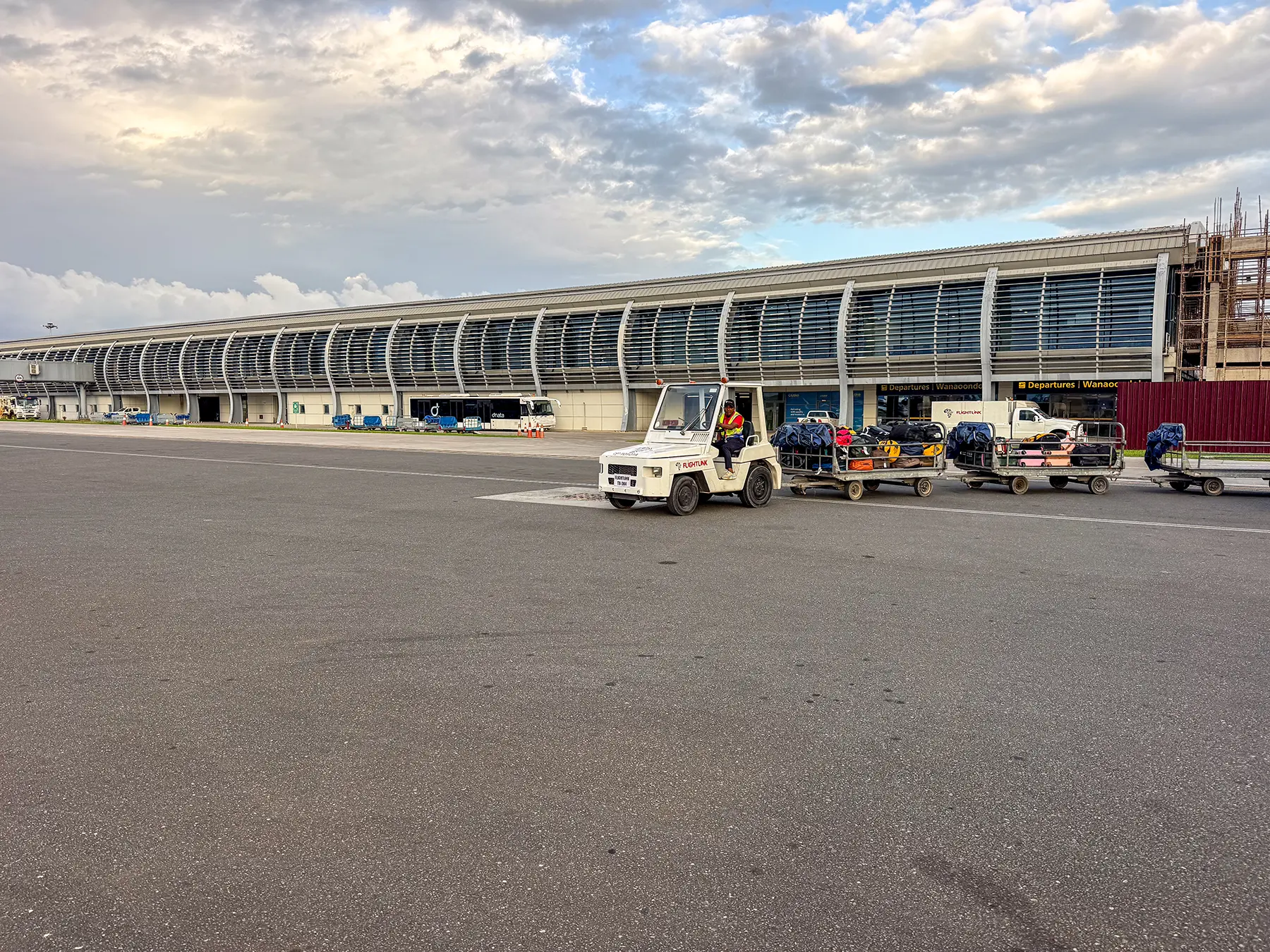 Baggage tractor towing loaded trailers past the long terminal building at Zanzibar Airport in Zanzibar, Tanzania